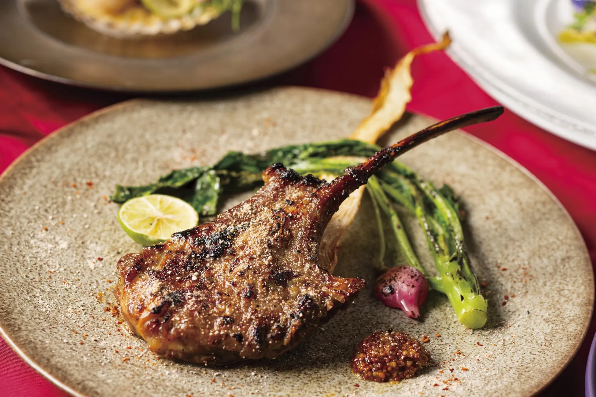 お皿に盛られたラムチョップの料理。焼き目がついており、付け合わせとしてライム、野菜、ソースが添えられている。